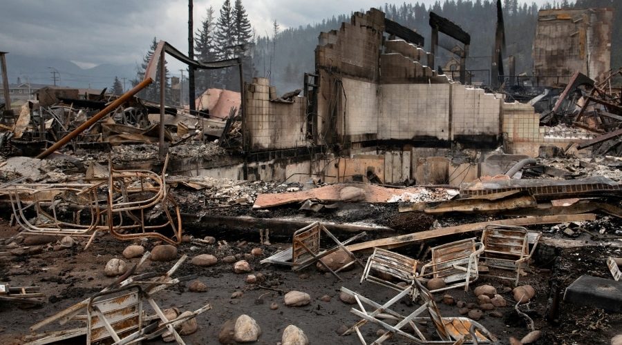 Burned residential structures and debris after a wildfire, showing cleared lots and stalled rebuilding in an urban neighborhood during post-fire recovery.