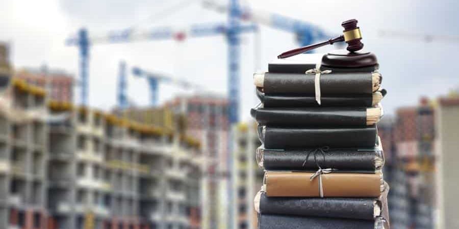 Stack of legal documents with a judge's gavel in front of a construction site with cranes, symbolizing AI-related legal risks and compliance challenges in the construction industry in 2025.