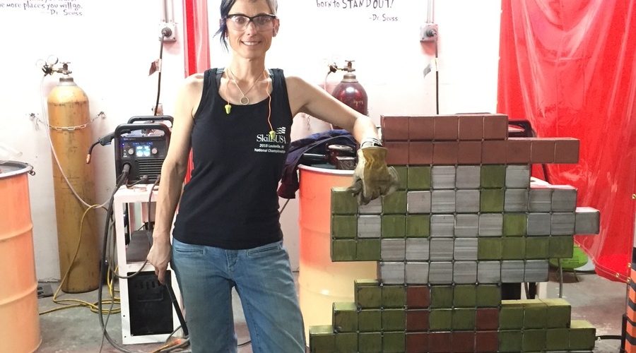 Welder Shanen Aranmor stands beside a pixel-art sculpture welded from painted steel blocks at her Weld Like a Girl shop in Yuma, Arizona.