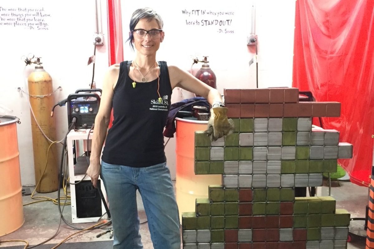Welder Shanen Aranmor stands beside a pixel-art sculpture welded from painted steel blocks at her Weld Like a Girl shop in Yuma, Arizona.